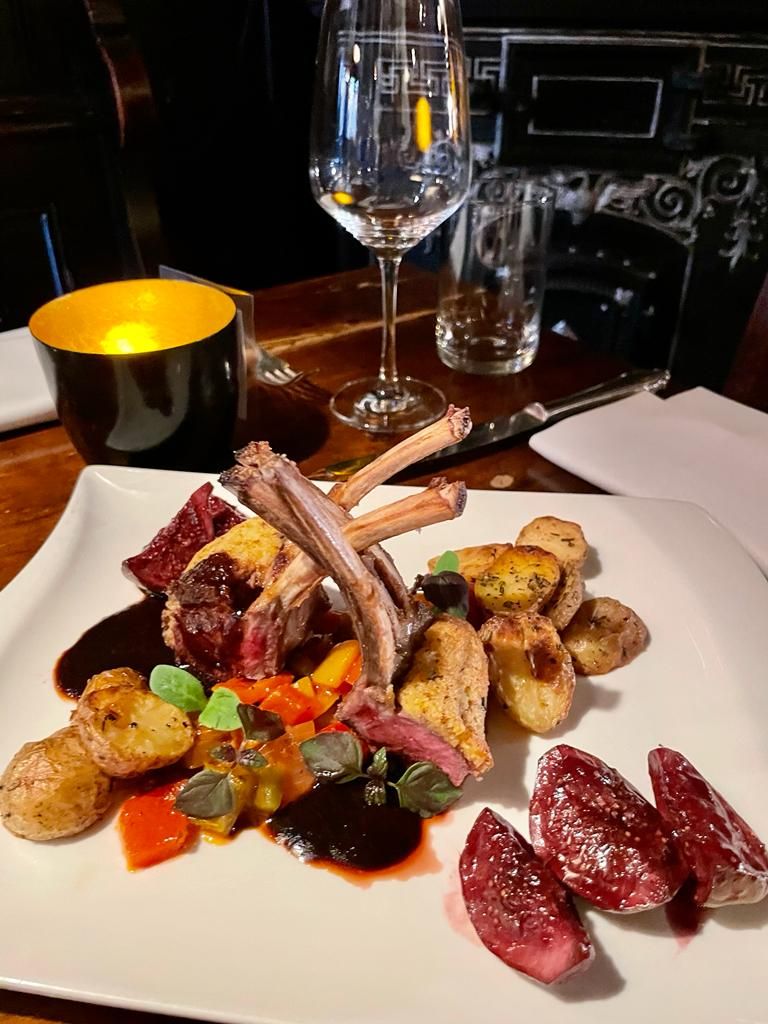 auf diesem Bild sieht man ein Teller Gericht mit gebratenem Lammkarree, dass appetitlich auf dem Teller angerichtet ist. Bei den Beilagen handelt es sich um buntes Gemüse sowie geröstete Rosmarin Kartoffeln.